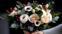 Elegant bouquet with blush roses, white anemones, red berries and eucalyptus leaves against dark background, romantic floral arrangement for weddings and celebrations.