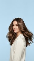 Young woman with flowing brown hair in motion wearing white shirt on light blue background for beauty and haircare advertising campaigns.