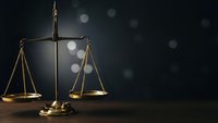 Golden scales of justice on dark background with bokeh lights representing legal system fairness and judicial balance in courtroom setting.