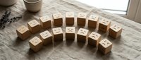 Wooden blocks with carved emoji faces arranged in a semicircle on linen fabric, showing emotions from happy to sad for mood and mental health concepts.