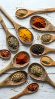 Colorful spices and herbs in wooden spoons on rustic white background. Culinary ingredients including turmeric, paprika, pepper for cooking and seasoning.