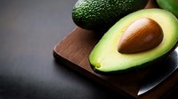 Fresh ripe avocado halves on wooden cutting board showing creamy green flesh and brown pit, healthy organic fruit for cooking and nutrition.