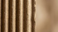Corrugated cardboard texture with natural brown color and vertical ridges showing detailed fiber structure for packaging and craft projects.