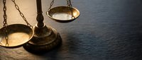 Brass scales of justice on dark wooden surface with dramatic lighting for legal and law firm concepts.