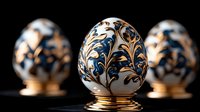 Decorative porcelain Easter eggs with elegant blue and gold floral pattern on black background. Traditional ornate design with delicate hand-painted details on golden stands.