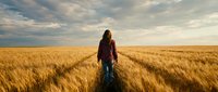 Young woman walking through golden wheat field at sunset with dramatic cloudy sky, peaceful rural landscape for agriculture and nature concepts.