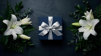 Elegant dark blue gift box with silver ribbon surrounded by white lilies and green foliage on dark slate background for special occasions and celebrations.