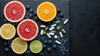 Fresh citrus fruits grapefruit orange lemon lime with blueberries and vitamin supplements on dark slate background for healthy nutrition concept.