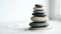 Balanced stack of smooth river stones in zen arrangement on textured surface with soft natural lighting for meditation and wellness concepts.
