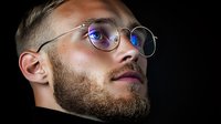 Portrait of bearded caucasian man wearing round glasses looking up thoughtfully against dark background, dramatic lighting highlights facial features and blue eye reflection.