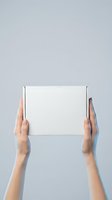 Female hands holding blank white cardboard box against gray background for product packaging mockup and shipping delivery concept.