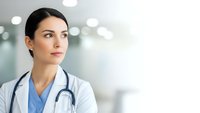Professional female doctor in white coat with stethoscope looking confidently ahead in modern medical facility for healthcare marketing materials.