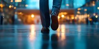 Person walking alone at night on wet city street with blurred bokeh lights creating moody urban atmosphere. Reflection on pavement adds cinematic feel.