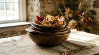 Rustic wooden bowls filled with colorful autumn leaves and dried flowers on burlap fabric near window. Cozy fall home decor and seasonal arrangement concept.