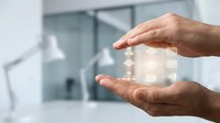 Hands holding transparent house symbol in modern office environment, representing real estate, property investment, home protection and business concepts.