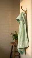 Soft green towel hanging on brass hook in modern bathroom with white subway tiles and wooden stool creating spa-like atmosphere for home decor.