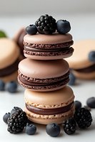 Stack of chocolate and vanilla macarons decorated with fresh blackberries and blueberries on light background, close up view of French pastry dessert.