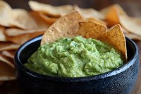 Fresh guacamole dip served in black stone bowl with crispy corn tortilla chips, close up view showing creamy avocado texture and appetizing presentation.