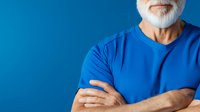 Senior Caucasian man with white beard wearing bright blue t-shirt standing with arms crossed against blue background, cropped portrait showing confidence and authority.