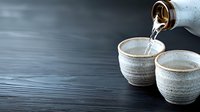 Pouring traditional sake from bottle into ceramic cups on dark wooden table with dramatic lighting and copy space. Japanese drinking culture.