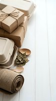 Eco-friendly packaging materials including cardboard boxes, biodegradable containers, kraft paper and wooden utensils on white wooden background.
