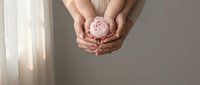 Woman hands gently holding pink crystal sphere in cupped palms against soft neutral background for meditation wellness and spiritual healing practices.