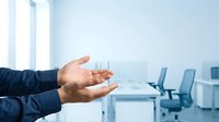 Business professional presenting in modern office conference room with glass of water and blue chairs.