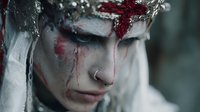 Young woman with crown of thorns and blood makeup for horror film or Halloween costume concept isolated on dark background.