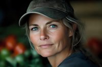 Middle-aged Caucasian woman wearing baseball cap smiles confidently at camera, natural lighting highlights blue eyes and gentle expression against blurred garden background.