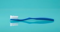 Blue toothbrush with white bristles on turquoise background for dental hygiene and oral care concepts.