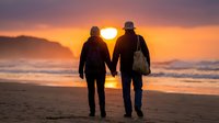 Romantic senior couple holding hands walking on beach at sunset with golden sky and ocean waves creating peaceful moment for love and retirement lifestyle.