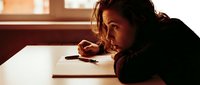 Young male artist with dark hair and olive complexion concentrating intently while sketching on white paper with pencil at wooden table, warm studio lighting.