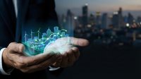 Businessman holding holographic green energy city with wind turbines and solar panels, sustainable urban development and renewable power technology concept.