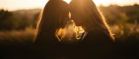 Two women sharing intimate moment with foreheads touching during golden hour sunset, romantic connection and love concept for relationship content.