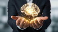 Businessman holding glowing brain hologram with golden light effects representing artificial intelligence, innovation and mental power in modern office.