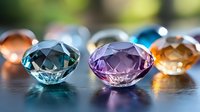 Collection of colorful cut gemstones including blue, purple and amber crystals arranged on reflective surface with soft bokeh background lighting effects.