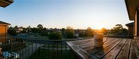 Panoramic view from a wooden balcony at golden sunrise, with a ceramic mug on the railing overlooking a peaceful suburban neighborhood.