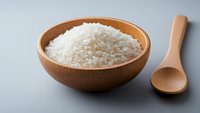 White rice grains in wooden bowl with spoon on gray background for healthy cooking and meal preparation concepts.