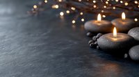 Glowing candles in stone holders on dark background with bokeh lights create peaceful spa atmosphere for wellness and meditation practices.