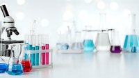 Modern laboratory setup with microscope and colorful chemical solutions in glass beakers and test tubes for scientific research and experimentation.