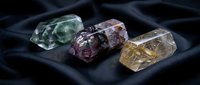 Three raw uncut gemstones displaying natural crystal formations on dark fabric surface for jewelry making and mineral collection purposes.