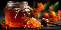 Golden honey in glass jar with wooden dipper and honeycomb on dark slate surface with orange marigold flowers in soft focus background for natural food photography.
