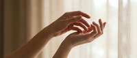 Two hands with medium-dark skin tone positioned together in a gentle, open gesture against soft natural light, conveying care, support, or connection for wellness and relationship concepts.