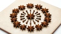 Star anise and cloves arranged in decorative circular pattern on wooden board for culinary design and cooking projects.
