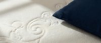 Closeup of embossed decorative swirl pattern on cream fabric with navy blue pillow corner, showcasing textile design and home decor details.