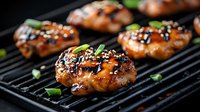 Grilled chicken thighs glazed with teriyaki sauce and sesame seeds on black grill grates, garnished with fresh green onions, dark moody food photography.