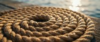 Coiled nautical rope on wooden dock with sparkling water background, maritime equipment for sailing and boating adventures.