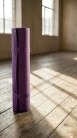 Purple yoga mat rolled up on wooden floor in sunlit studio room with windows for fitness and meditation practice.