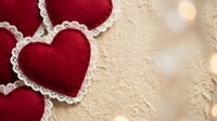 Red felt hearts with white lace trim on wooden background with warm bokeh lights for Valentine's Day romance and love celebration decorations.