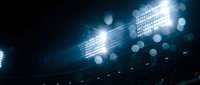 Bright stadium floodlights illuminating sports arena with dramatic lens flares and bokeh effects against dark night sky for athletic events and competitions.